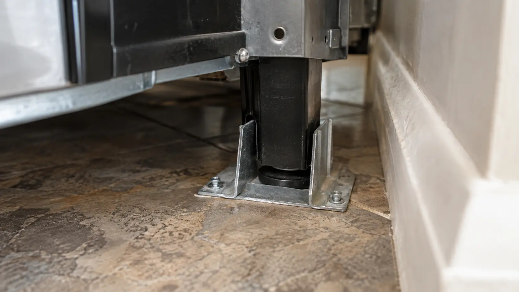 Close on a range's rear leg sitting inside its floor anti-tip bracket.