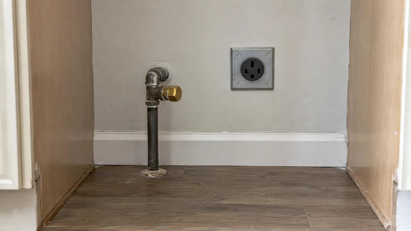 Close on a capped gas stub beside a heavy-duty outlet behind a range space.