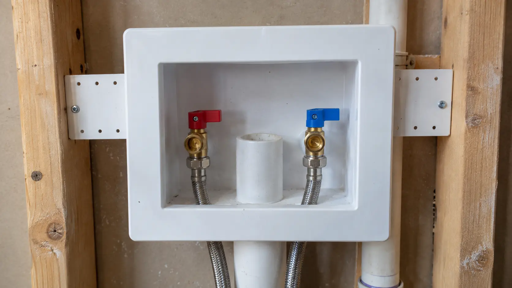Close on a laundry box in a wall with hot and cold valves and a drain opening.