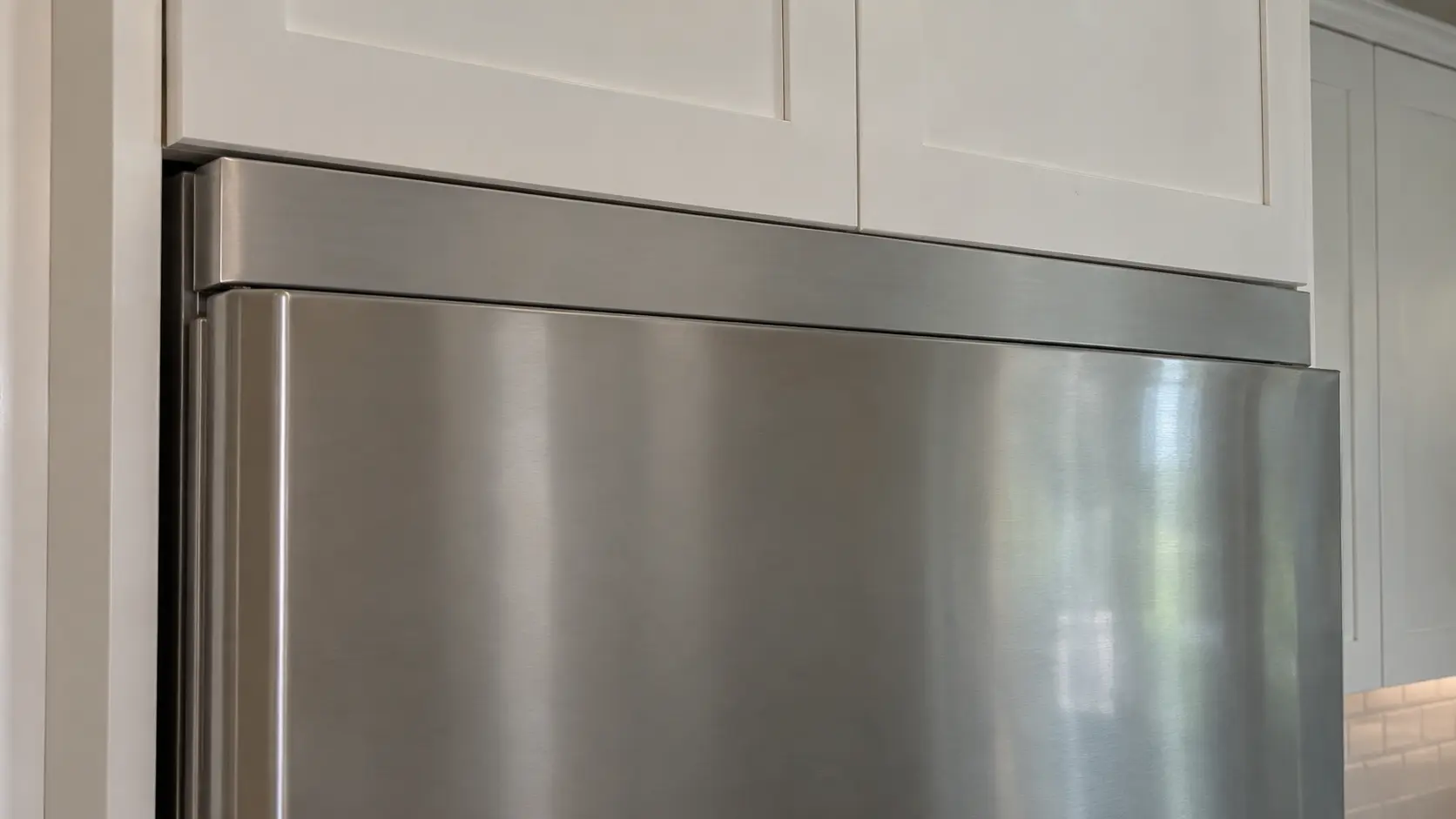 Close on a built-in refrigerator's top trim touching the cabinet above.